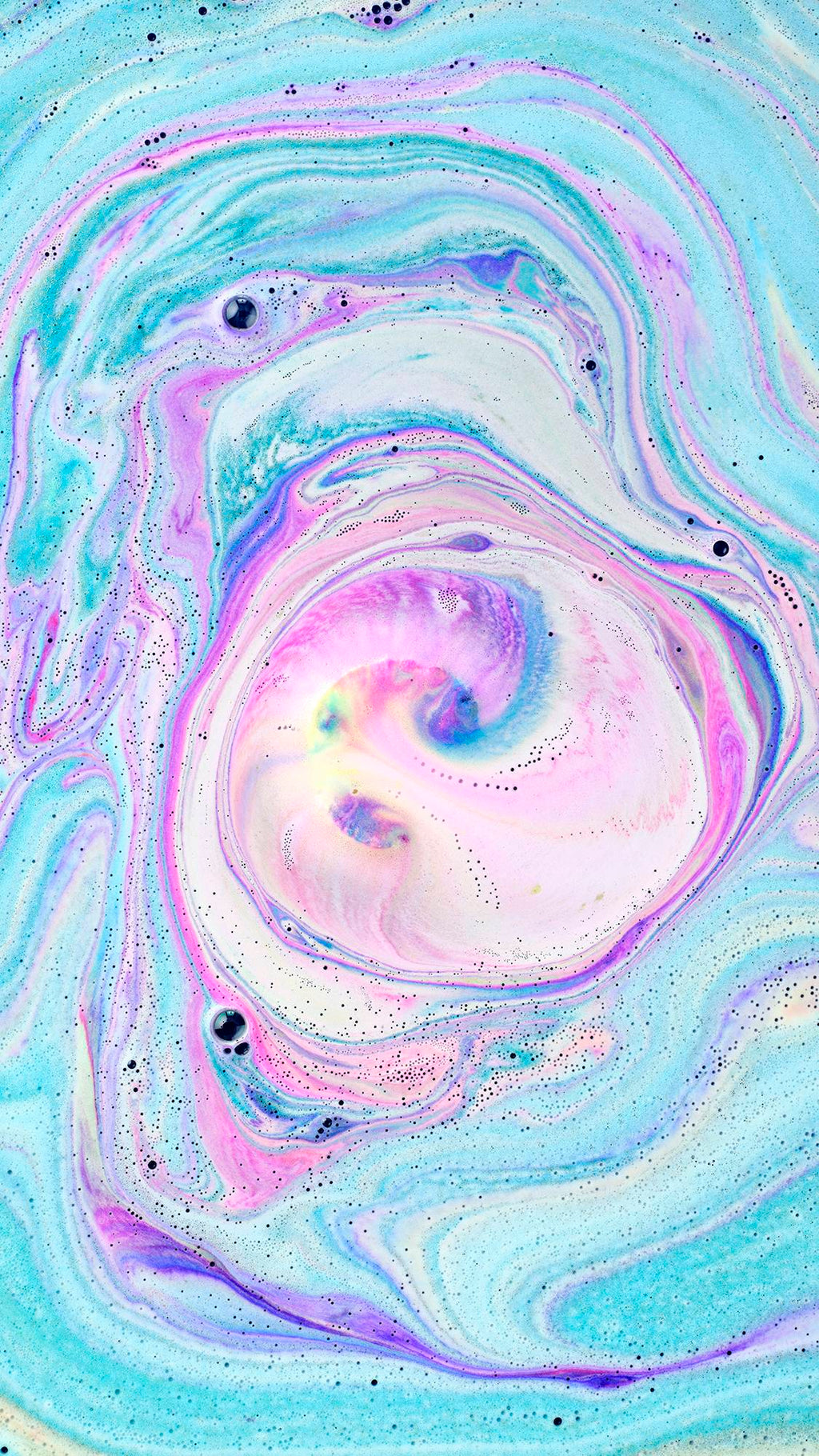 A top-down view of bathwater featuring a mesmerizing swirl of vibrant neon pink, bright blue, and soft white foam. The colors create a cosmic, marble-like pattern with tiny dark speckles scattered throughout the water's surface.
