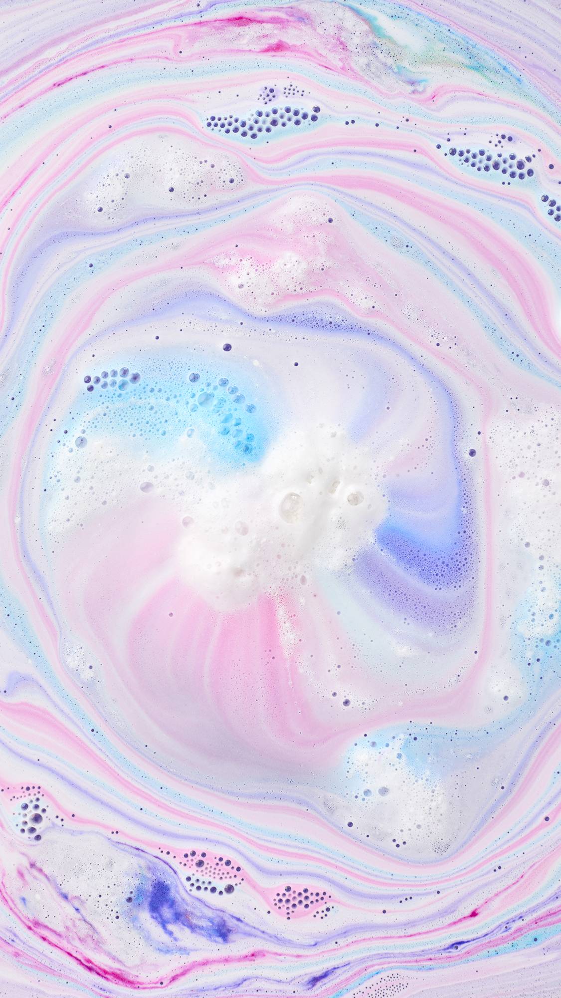 Top-down view of Toby's Magic Cow Bath Bomb dissolving, creating a mesmerizing swirl of pastel pink, blue, and purple foam across the water.