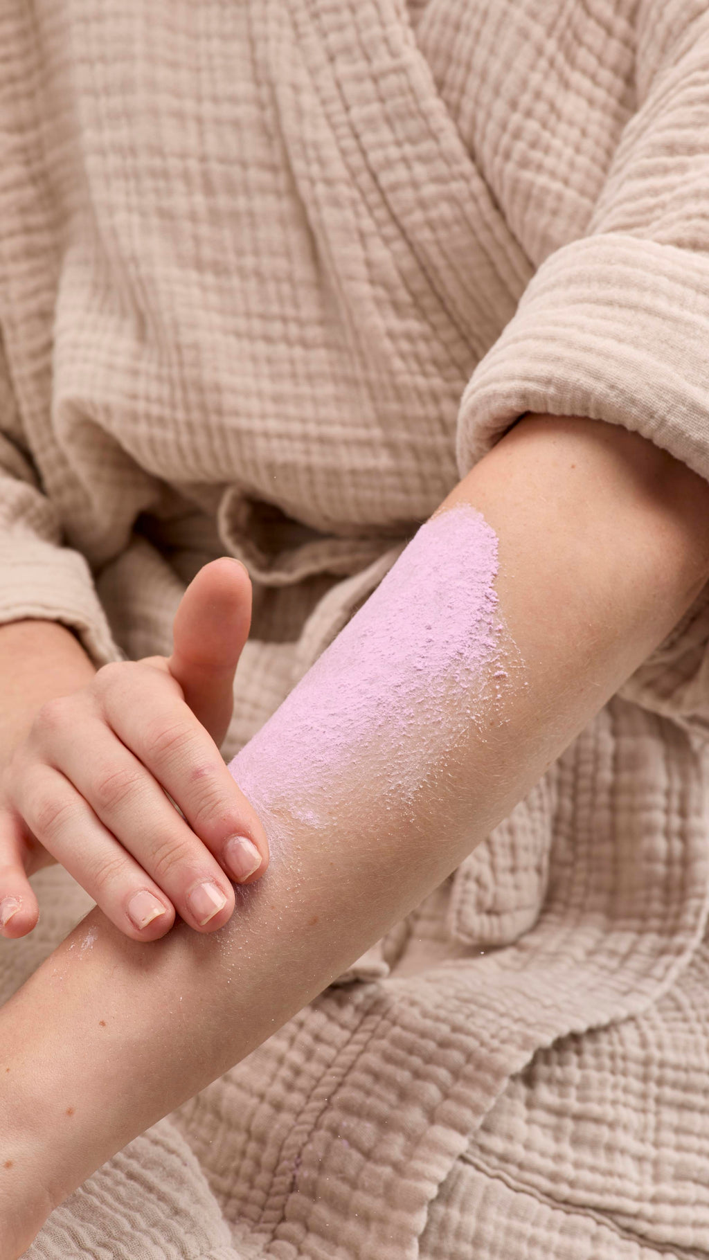 The image shows a hand rubbing a broad smear of pale purple 'Sleepy Dust' dusting powder onto a bare forearm. The person wears a light-coloured robe against a beige background.