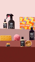 The Sticky Dates range is displayed on three coloured shelves. Products include hair primer, body spray, gift box, Lush Melt, bath bomb, shower gel, lip scrub, body lotion, and an open pot of body scrub.