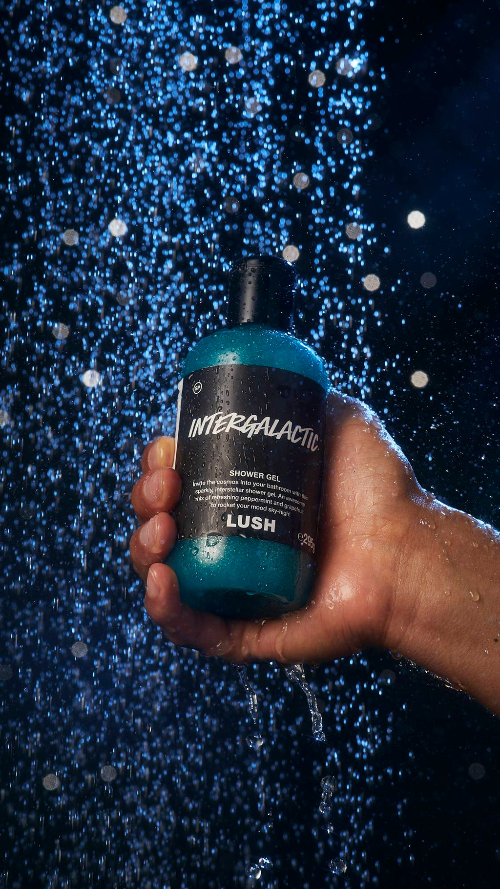 Image shows a model holding a bottle of the shower gel under a shower.