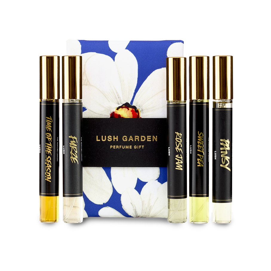 The image shows a "LUSH GARDEN" perfume gift set. Five thin, cylindrical glass perfume bottles with amber and clear liquids are arranged around a dark blue box featuring a large white floral design.
