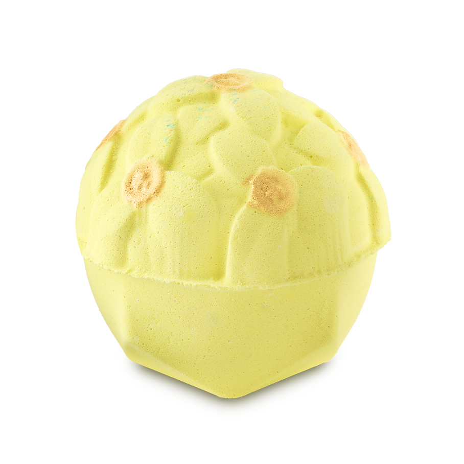 A pale yellow, dome-shaped bath bomb with a detailed floral pattern on top. Several of the molded flower centers are accented with a shimmering gold finish.