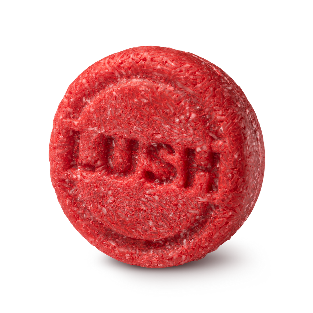 New shampoo. A circular, highly textured red solid shampoo bar. The fibrous, shredded surface features the brand name 'LUSH' embossed clearly in the centre of the round face.