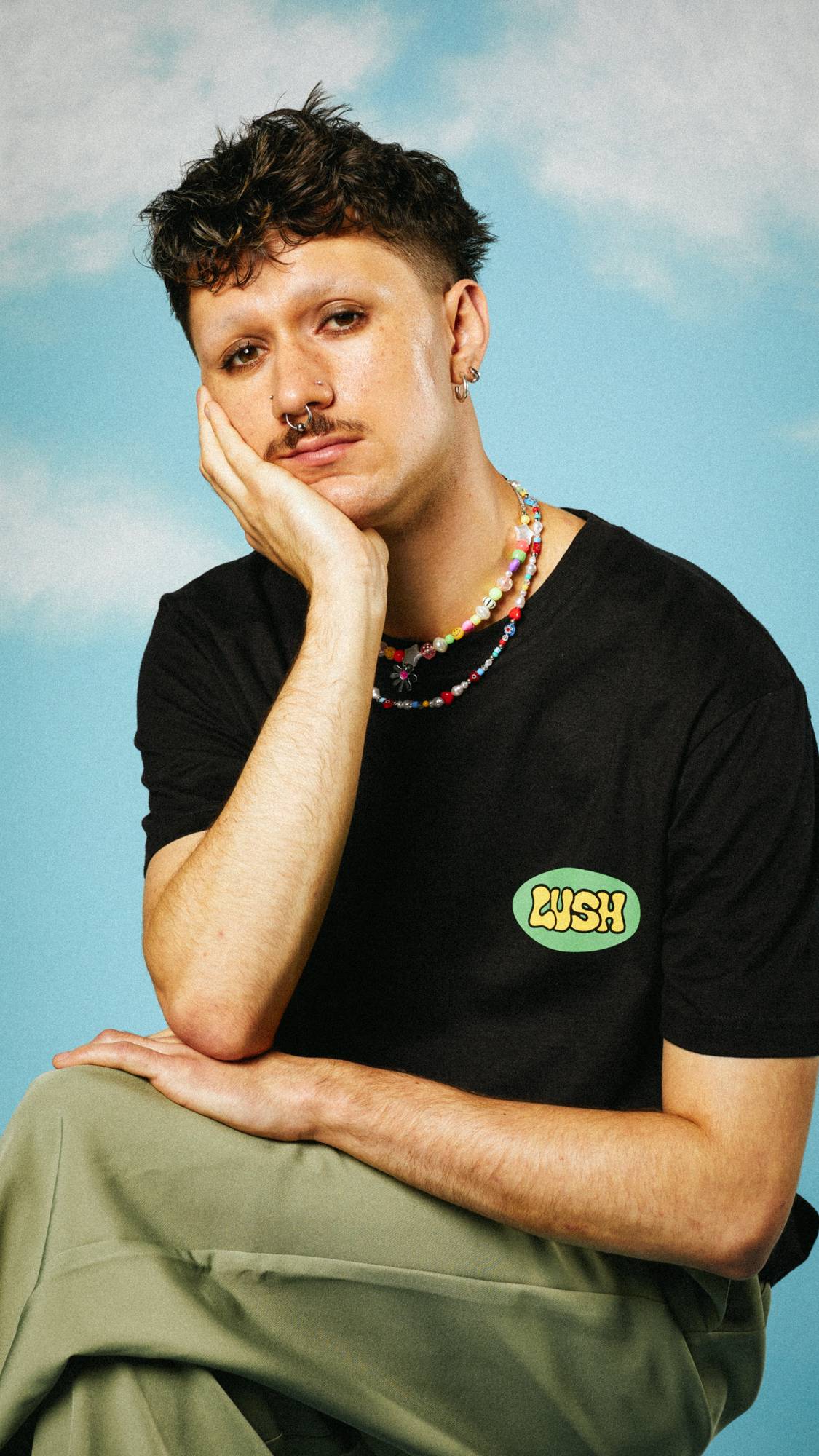 Model is sat with one leg over the other wearing the Retro Bubble t-shirt. They have a colourful beaded necklace.