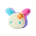 U.SA.HA.NA. A colourful bath bomb shaped like a bunny character's head with a cream face, blue eyes, and an orange flower. One ear is bright blue and the other is pink, with purple accents throughout.