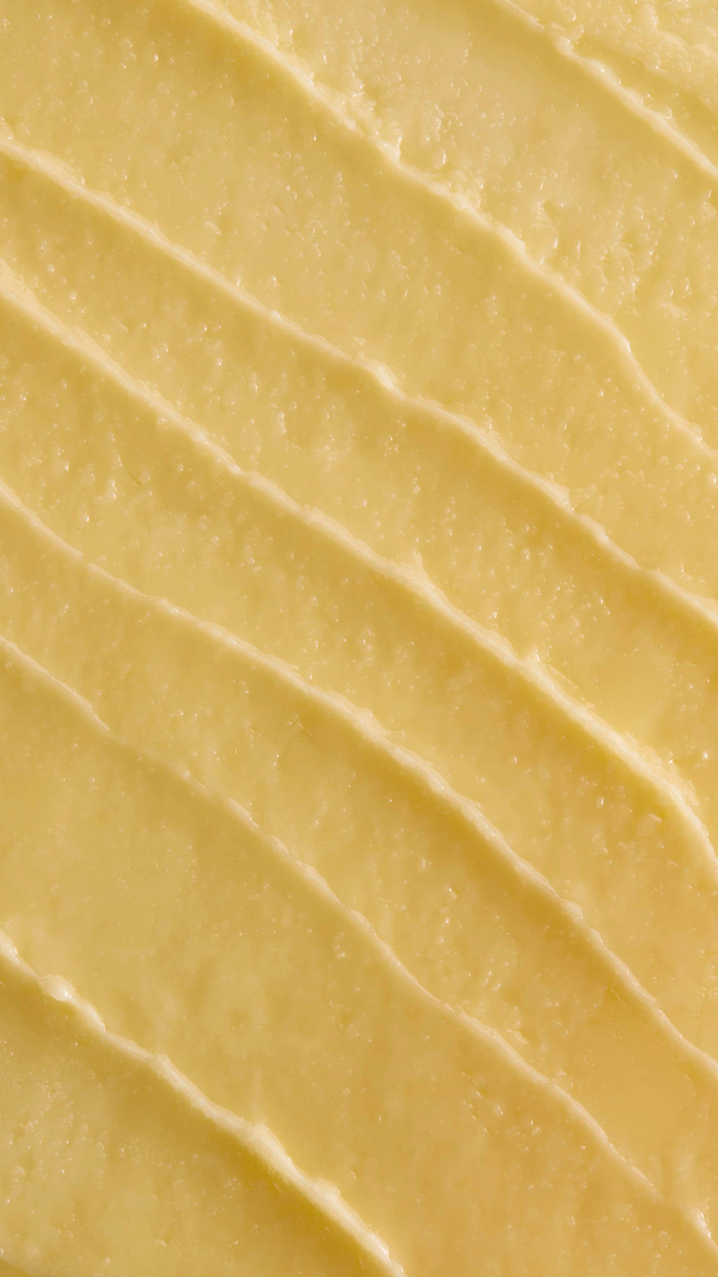 A close-up, aerial shot of thick, pale yellow 'Ultraplant' facial cleanser. The product is spread out in several diagonal, textured ridges, showing its smooth yet slightly granular, buttery consistency.